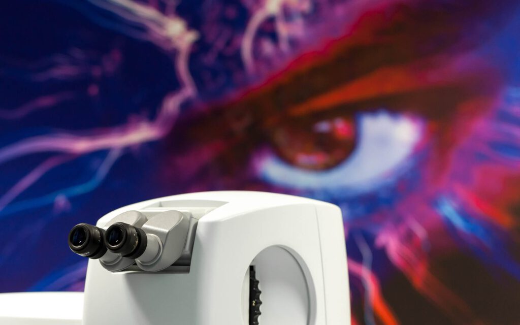 Lasergerät im 5. Obergeschoss der Praxis; im Hintergrund ein Kunstmotiv mit Auge, das die Verbindung von Technik und Sehen symbolisiert.