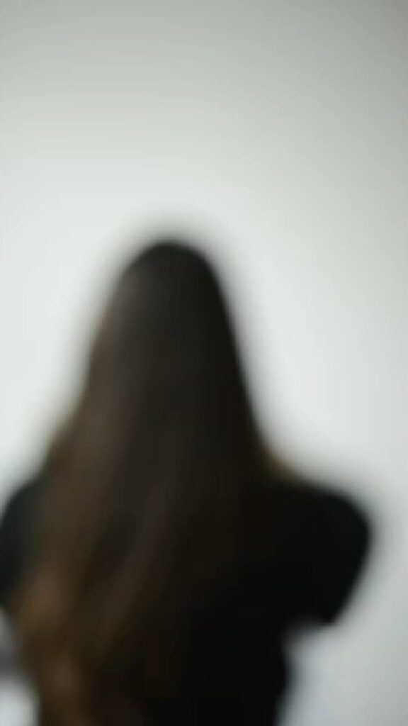 Unscharfe Aufnahme einer Person mit langen Haaren von hinten; künstlerische Darstellung in neutralem Raum.