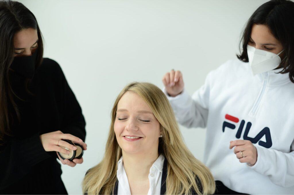 Zwei Personen stylen eine Frau mit blondem Haar während des Fotoshootings; entspannte Stimmung und helles Raumlicht.