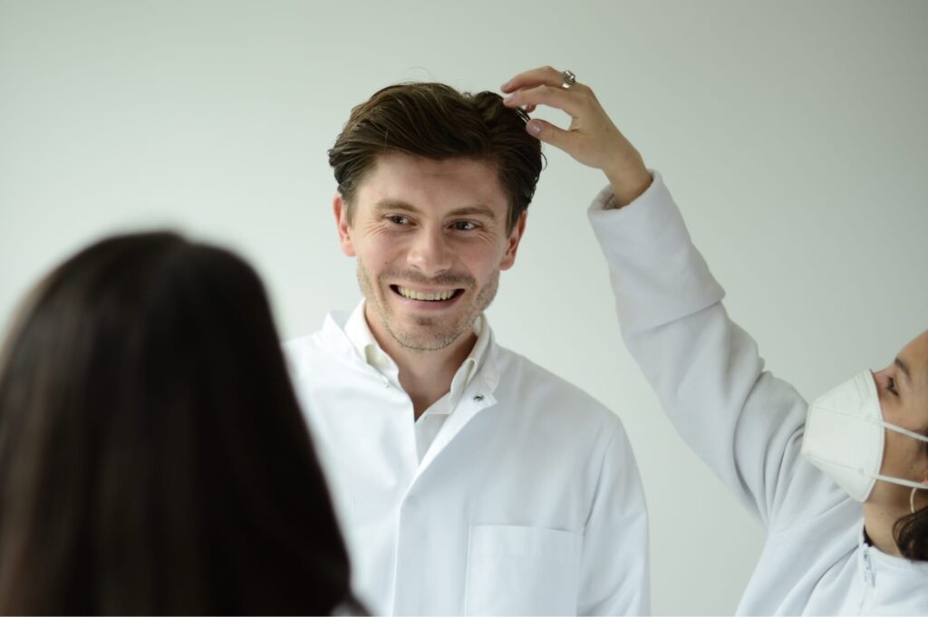 Porträtaufnahme von I. Fischinger beim Fotoshooting; lächelnd, während das Team letzte Handgriffe an Frisur und Kleidung vornimmt.