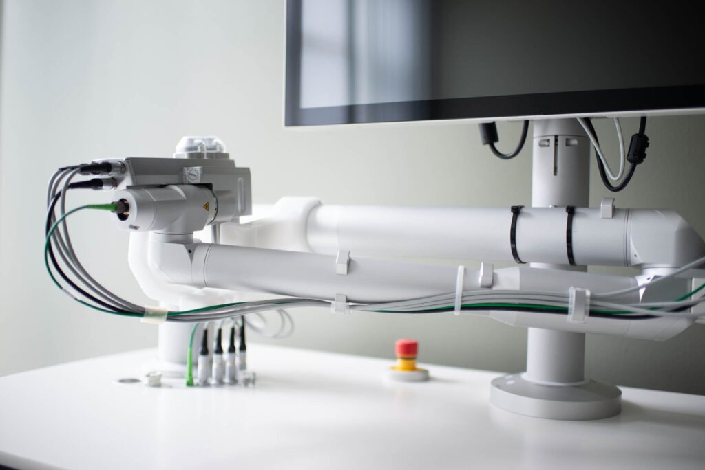 Detailaufnahme des Ziemer-Femto-Lasers; zeigt den schwenkbaren Arm mit Leitungen und Bedienelementen im Untersuchungsraum.